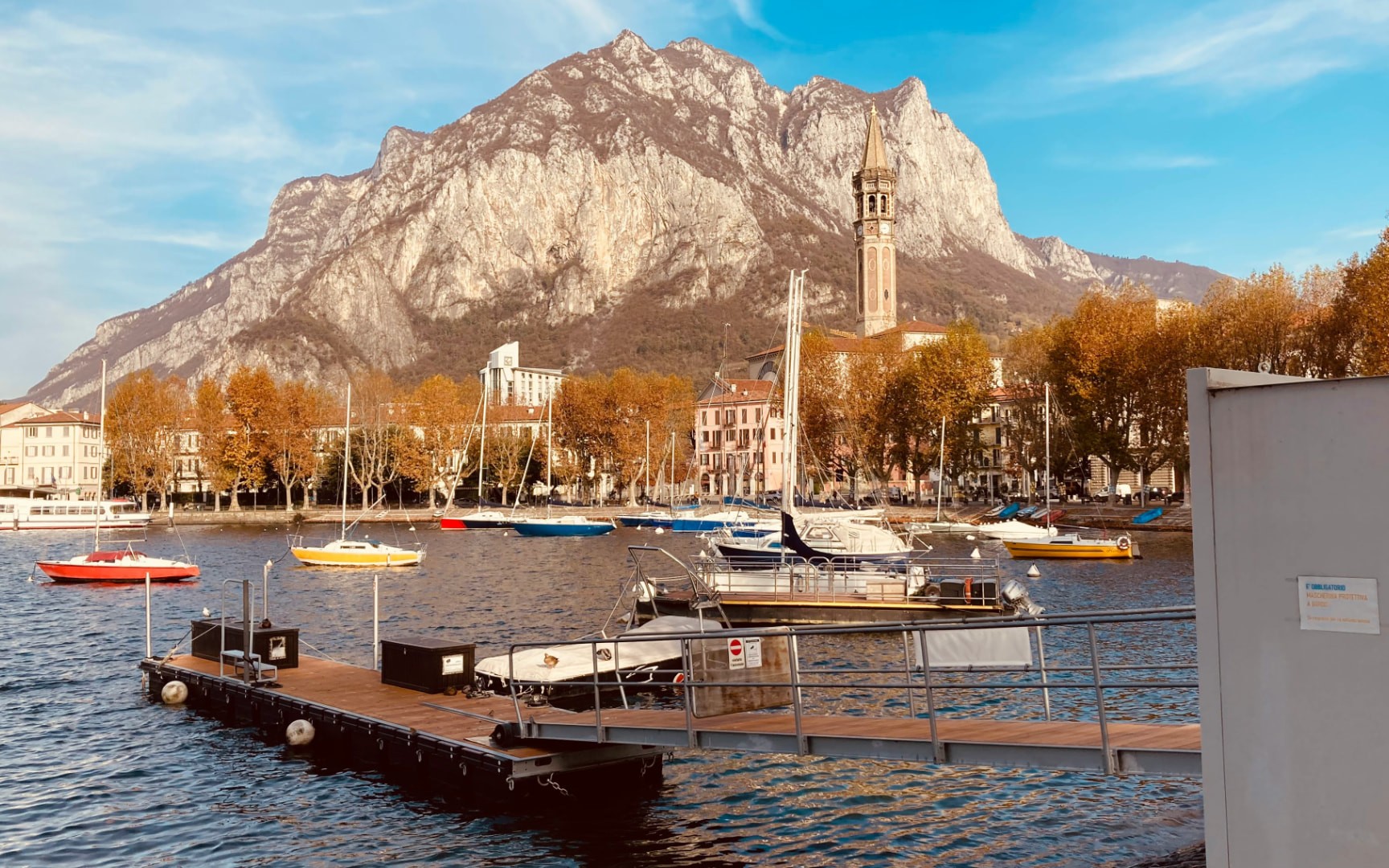 Lecco lakefront with boats, the old town bell tower and the mountains of Lake Como